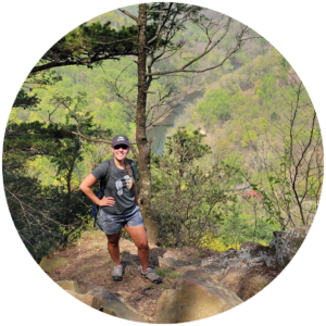 hiker poses in front of overlook with creek in background